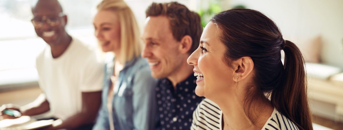 Diverse group of businesspeople laughing while sitting in a row together during a presentation in an office